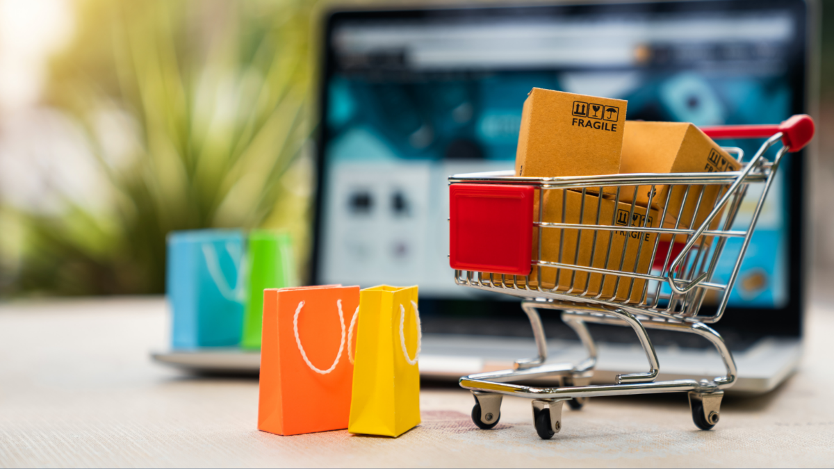 Mini shopping cart with packages and shopping bags in front of a laptop